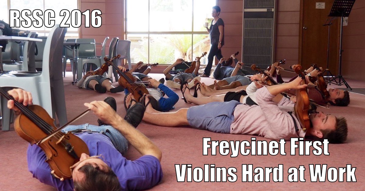 Violinists playing while lying flat on the ground in the Camp Clayton Dining Room, with tutor Joanna Drimatis. Caption in Impact Typeface says "RSSC 2016 Freycinet First Violins Hard at Work".